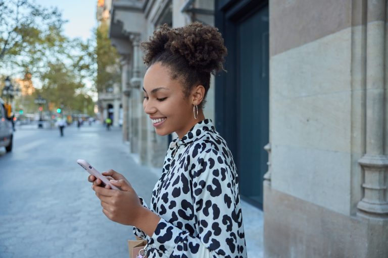 Smiling woman using smartphone on city street.