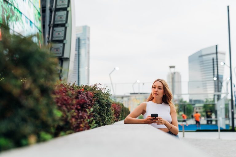Woman sitting outdoors with smartphone in urban area.